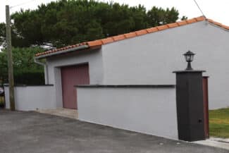 Maison et garage à porte rouge derrière un mur de clôture
