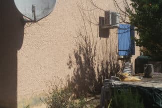 Façade ocre ombragée par un arbre avec volets bleus