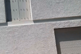 Bas de façade en crépi gris à côté d'une porte de garage