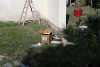 Matériel de chantier posé dans un jardin devant un mur à traiter