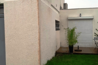 Façade beige avec porte de garage blanche et massif de plantes
