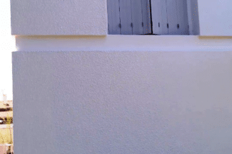 Pan de mur en enduit gris clair lisse sous une fenêtre