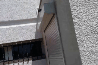 Angle de maison en crépi clair avec volet roulant