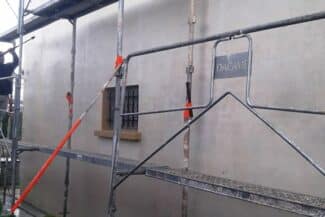 Façade en travaux avec tuyaux et échafaudage au pied du mur