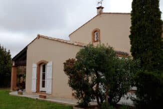 Maison beige et sa toiture en tuiles entourées de végétation à Tournefeuille
