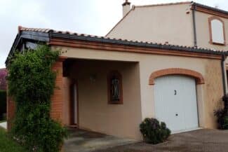 Façade beige avec porte de garage et végétation à Tournefeuille