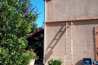 Échelle le long d'une façade crépie avec descente pluviale