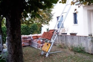 Échelle dressée contre une maison, matériaux au sol