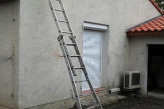 Échelle posée contre un mur blanc près d'une porte de garage