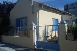Portail et piliers devant une maison aux volets bleus