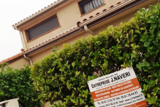 Maison avec panneau de chantier devant une haie